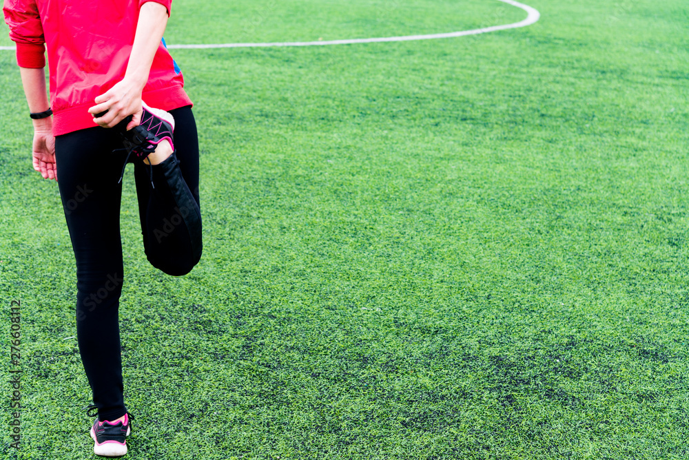 Fototapeta premium Girl in black sports leggings and a pink jacket kneads before training in an open sports arena