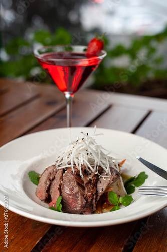 Top view of thai style marbled beef salad with sweet alcoholic strawberry cocktail on summer terrace
