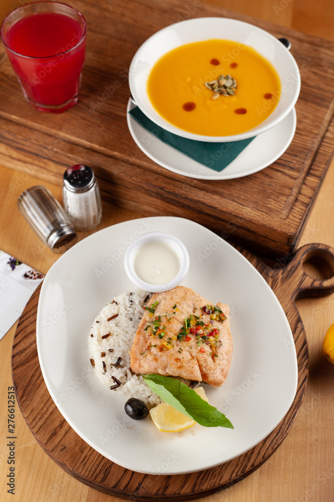 Two course lunch in a restaurant, served on a wooden table: steamed salmon and rice, bright-yellow spicy pumpkin soup