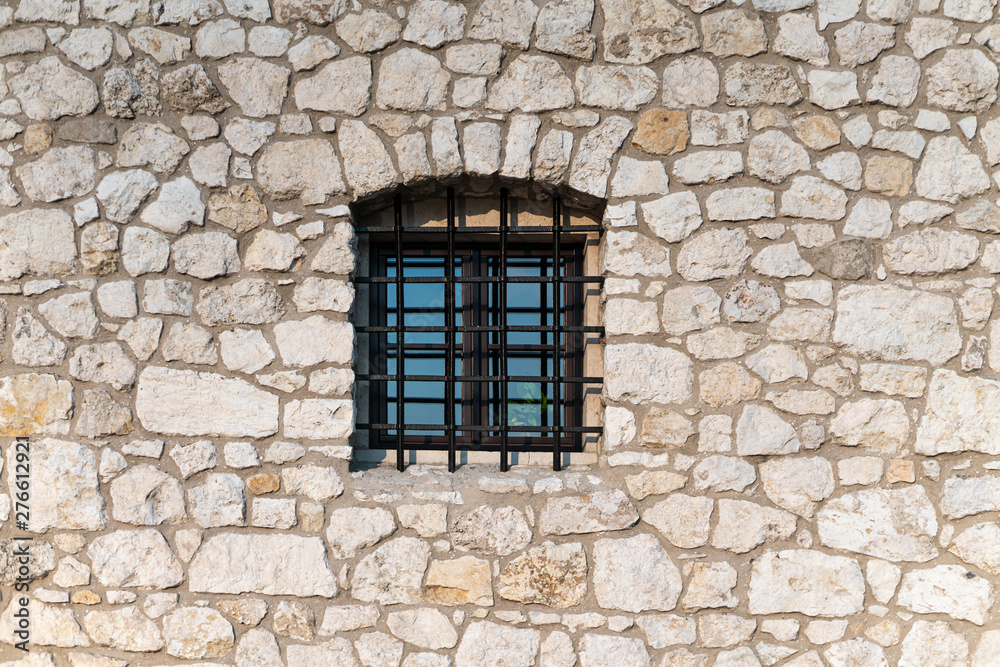 Wall made of limestone with a window with a grate.