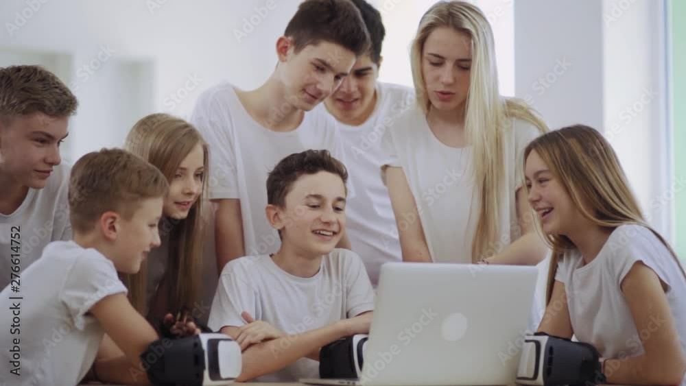 group of attractive teen students in white t-shirts using a computer laptop in a school library. happy classmates laughing together watching cool videos during a break. group of attractive teen students in white t-shirts using a computer laptop in a school library. happy classmates laughing together watching cool videos during a break.