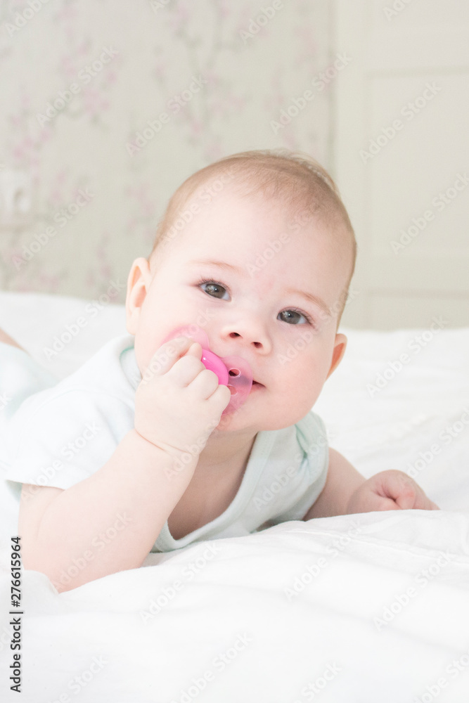 Baby girl portrait close-up vertical. The baby's face is 6 months old, lying on his stomach, pulling the nipple in his mouth. Baby girl portrait close-up vertical. The baby's face is 6 months old, lying on his stomach, pulling the nipple in his mouth.