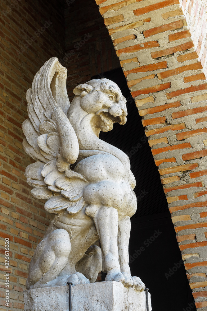 side view of a gargoyle carved in stone with a wall of bricks as background