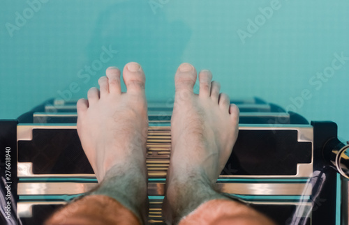 Man with bare feet descending on the ladder in the pool .