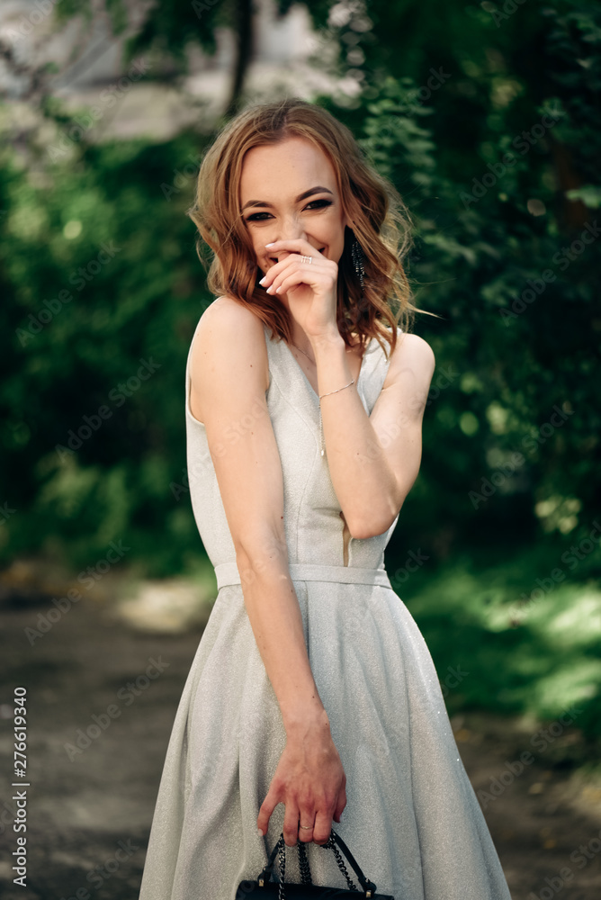 Gorgeous young model woman with perfect  hair looking at camera posing in the city wearing  evening dress.