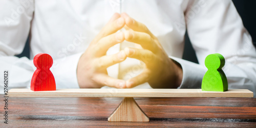 A man with hands in the gesture of a lock and looks at the red and green standoff figures on a scales. conflict resolution and the search for a compromise in the dispute. Thoughtful decision