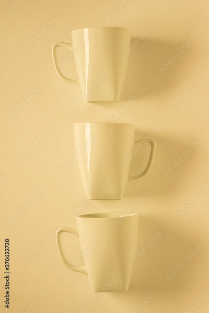 3 yellow coffee mugs on yellowish background in a vertical row, empty copy space 3 yellow coffee mugs on yellowish background in a vertical row, empty copy space