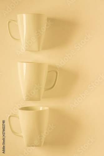 3 yellow coffee mugs on yellowish background in a vertical row, empty copy space