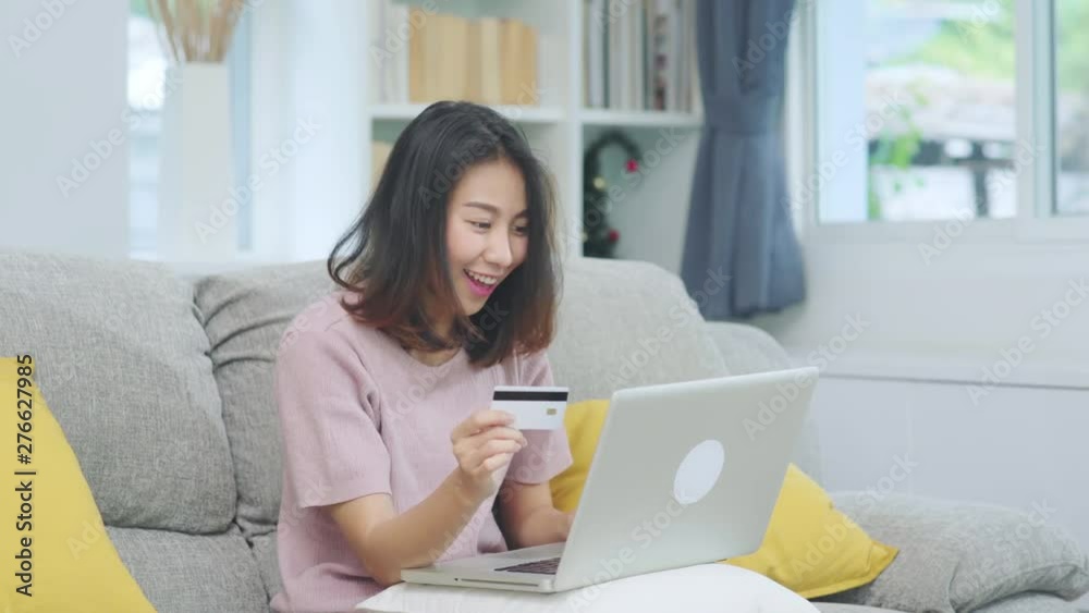 Asian woman using laptop and credit card shopping ecommerce, female relax feeling happy online shopping sitting on sofa in living room at home. Lifestyle women relax at home concept. Asian woman using laptop and credit card shopping ecommerce, female relax feeling happy online shopping sitting on sofa in living room at home. Lifestyle women relax at home concept.