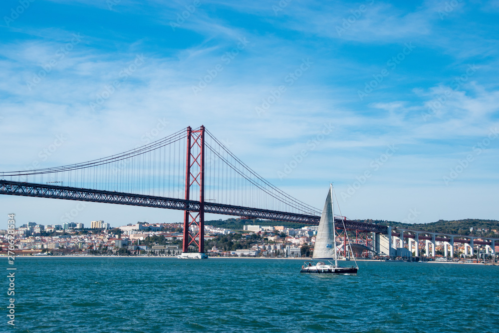 The 25th of April brige over the River Tagus with a sailboat in Lisbon, Portugal