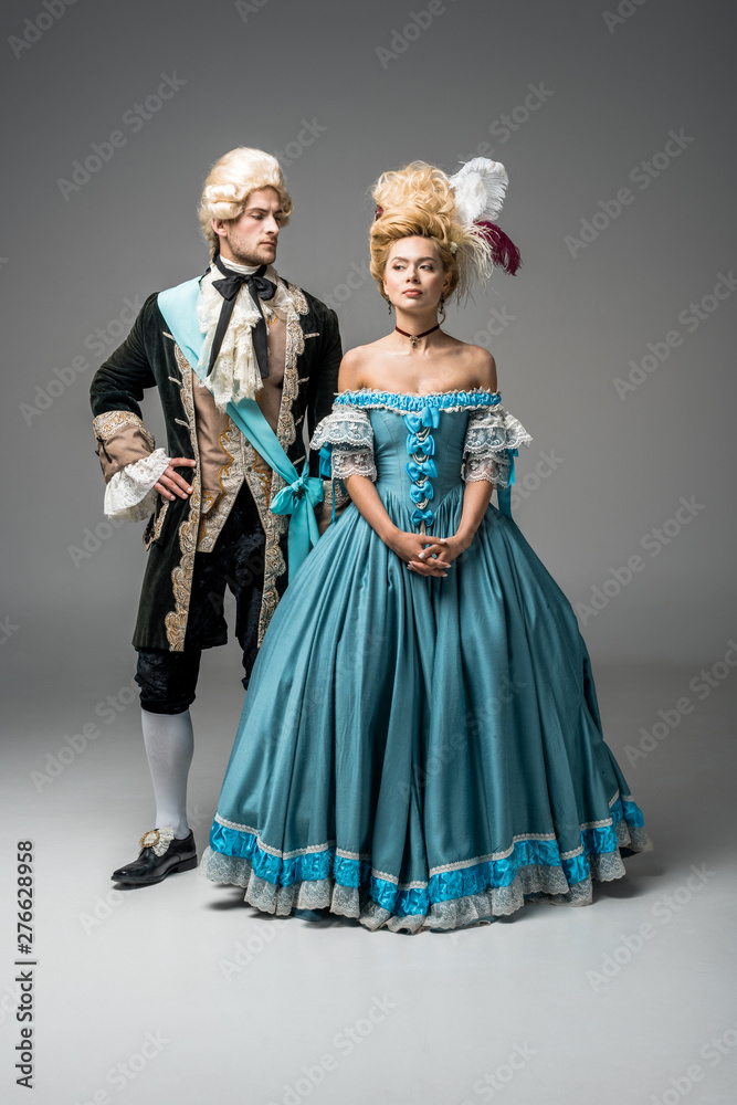 attractive victorian woman in blue dress near handsome man with hand on hip on grey
