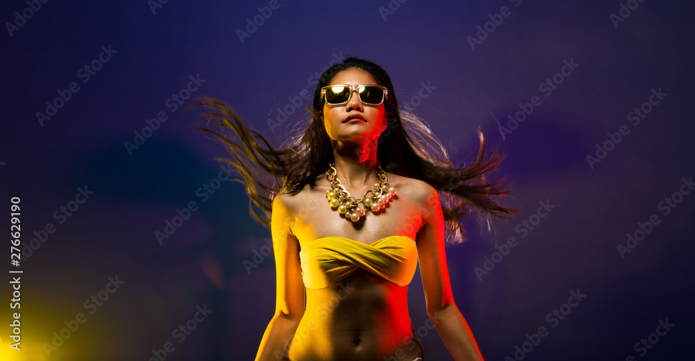 Fashion Asian Woman Tan skin black hair beautiful high fashion make up sunglasses pearl necklace accessories wear yellow bikini. Studio Lighting Dark smoke Background copy space text logo Fashion Asian Woman Tan skin black hair beautiful high fashion make up sunglasses pearl necklace accessories wear yellow bikini. Studio Lighting Dark smoke Background copy space text logo