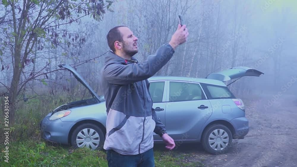 man searching for a mobile network in front of a broken car. Autumn or spring forest. man searching for a mobile network in front of a broken car. Autumn or spring forest.