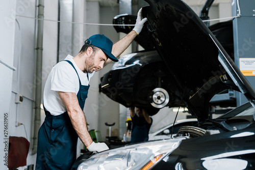 selective focus of bearded car mechanic in gloves looking at car engine