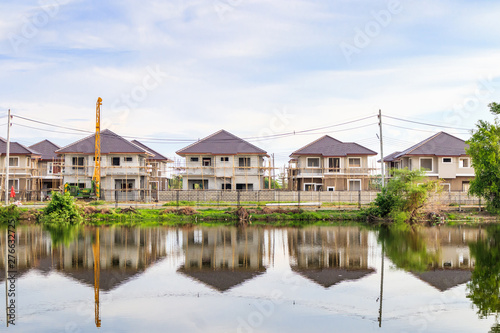 New house building reflection with water in lake at residential estate construction site with clouds and blue sky