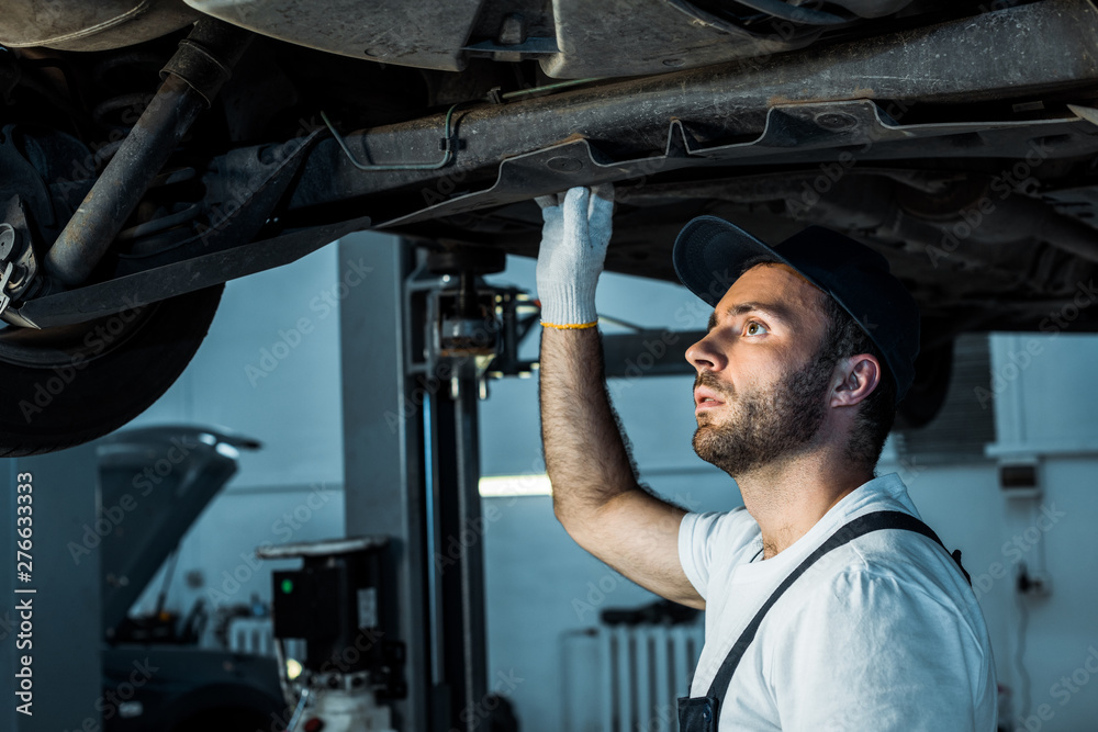 bearded car mechanic in cap repairing automobile in car service bearded car mechanic in cap repairing automobile in car service
