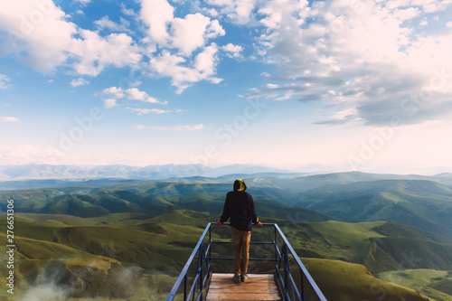 Travel man tourist alone on the edge viewing platform or observation point made from metal over amazing epic valley mountains adventure lifestyle extreme vacations green landscape
