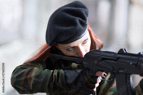 A young girl with a green camouflage uniform and a black beret with a gun among the ruins. Girl warrior with weapons.