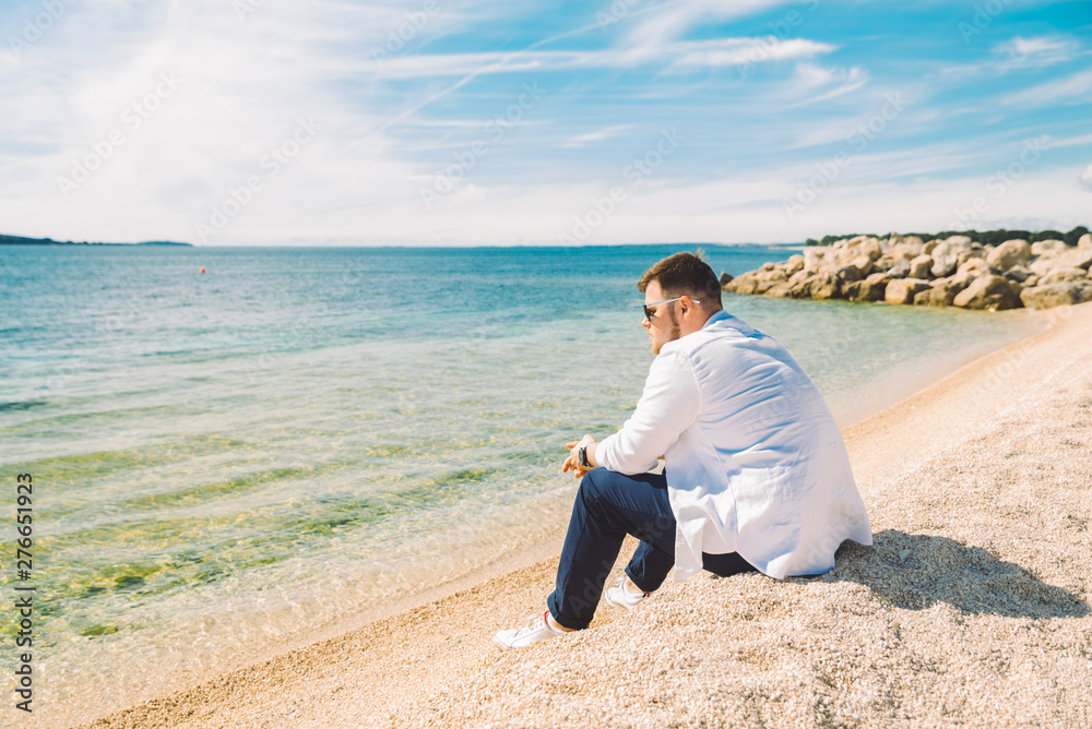 young stylish man sitting at sea beach enjoying the view young stylish man sitting at sea beach enjoying the view