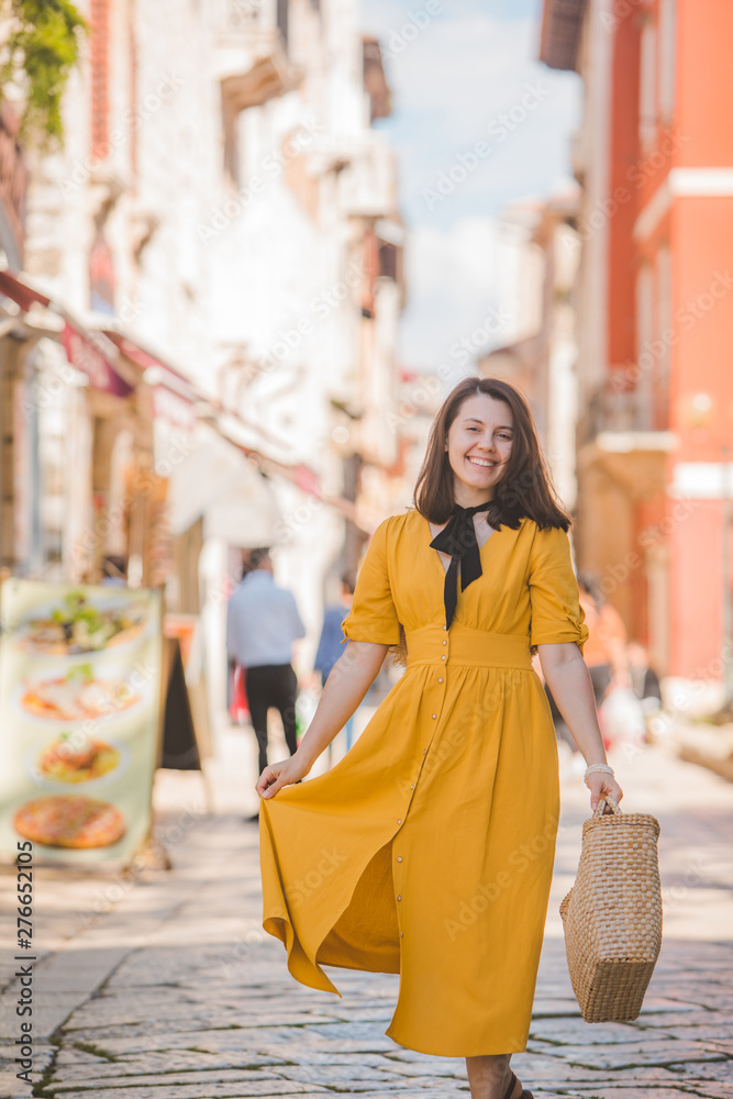 Fototapeta premium woman in yellow dress with bit straw hat walking by old tourist city in croatia