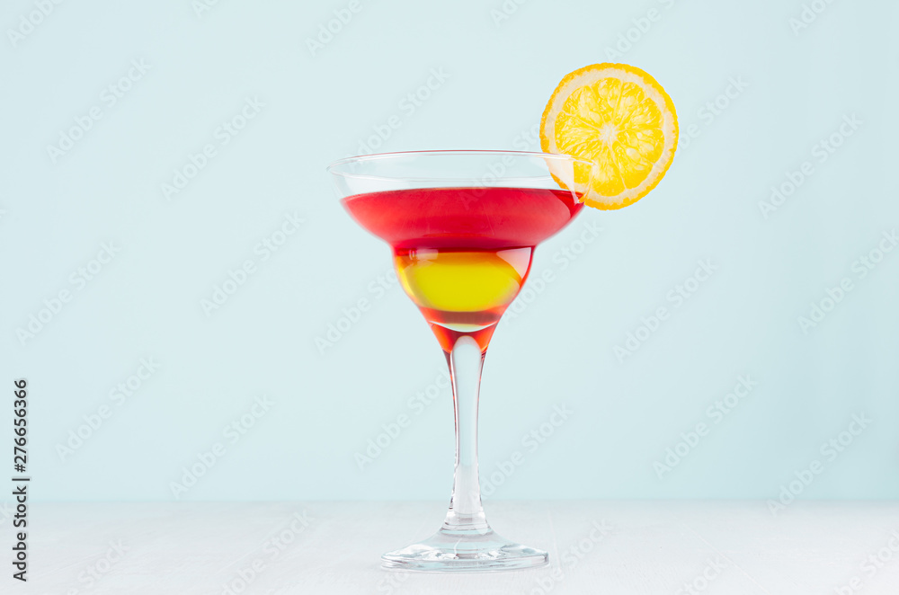 Summer fresh alcohol cocktail with red and yellow liquor, orange slice on soft light white and pastel green background. Summer fresh alcohol cocktail with red and yellow liquor, orange slice on soft light white and pastel green background.