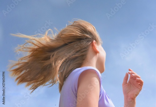 blonde girl runs and hair fluttering under blue sky