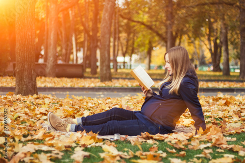Young pregnant girl reads a book sitting on a plaid in an autumn park. Concept of the onset of autumn and recreation in outdoor