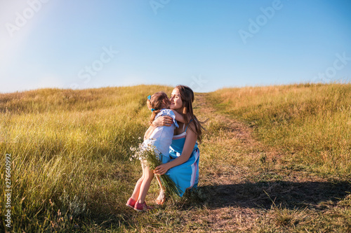 Young mother and daughter, hugging and playing in a golden field of sunshine.