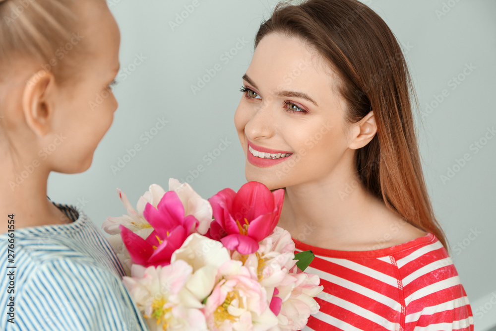 Little girl greeting her mother with bouquet of tulips on light background Little girl greeting her mother with bouquet of tulips on light background