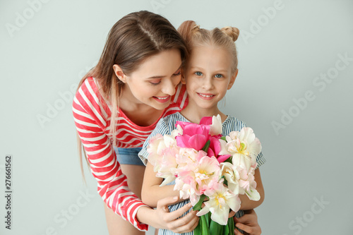 Little girl and her mother with bouquet of tulips on light background