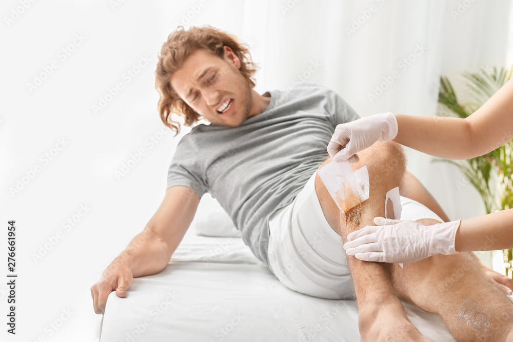 Man suffering from pain during wax epilation of legs in beauty salon Man suffering from pain during wax epilation of legs in beauty salon