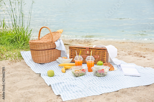 Wicker baskets with tasty food and drink for romantic picnic near river photo