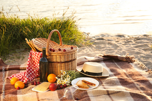 Fotografia Wicker basket with tasty food and drink for romantic picnic near river