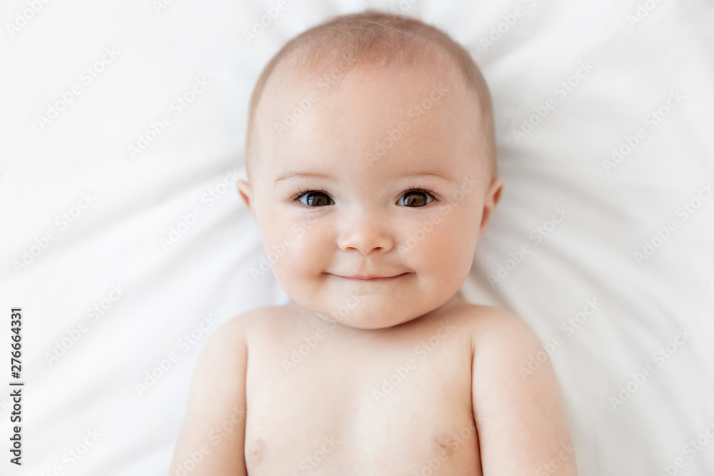 Close up portrait of smiling baby lying on white bed Close up portrait of smiling baby lying on white bed