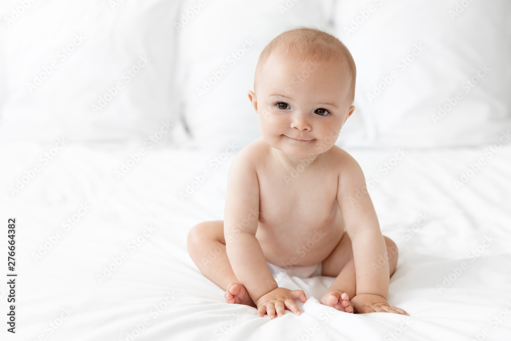 Smiling baby in diaper sitting on white bed