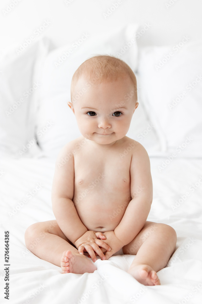 Smiling baby sitting on white bed Smiling baby sitting on white bed