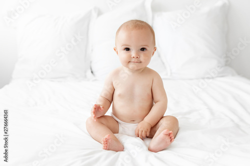 Baby in diaper sitting on white bed