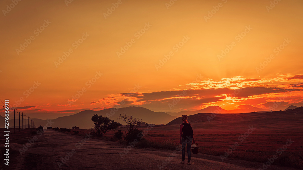 The girl goes on the road at sunset in the mountains