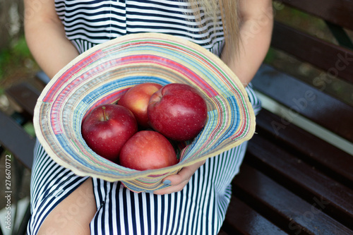 A girl sits on a bench and holds red apples with a hat photo