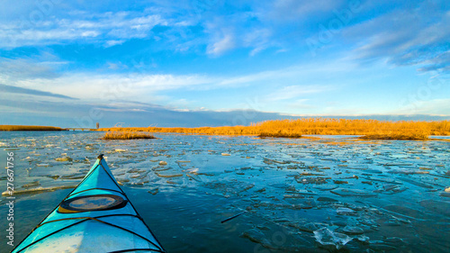 View from bow (prow) of blue kayak on lake with ice floes in winter or early spring at buatiful sunset. Winter kayaking photo