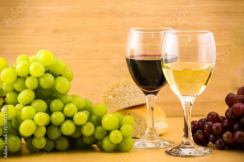 Red and white wine glass with green and red grapes with bread on a wooden table and wall 