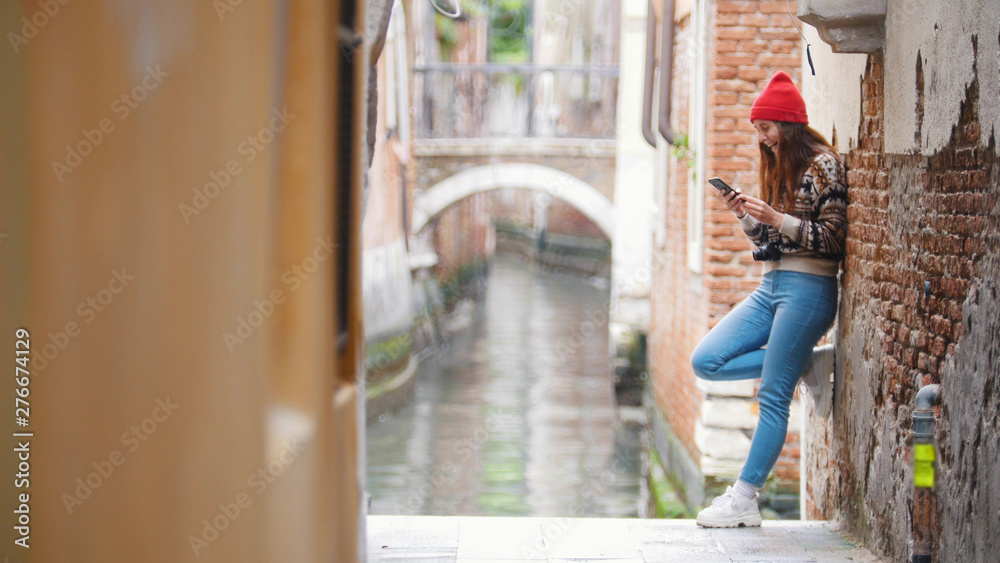 A young woman standing near the water channel and searching for something in her phone - Venice, Italy