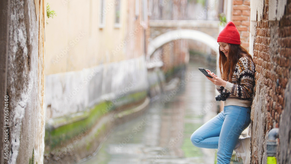 A young woman standing near the water channel and looking in her phone - Venice, Italy