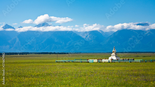 Siberian Tunka valley on the background of Eastern Sayan Mountains in summer sunny day. The Buddhist Stupa in green meadow. Beautiful landscape photo