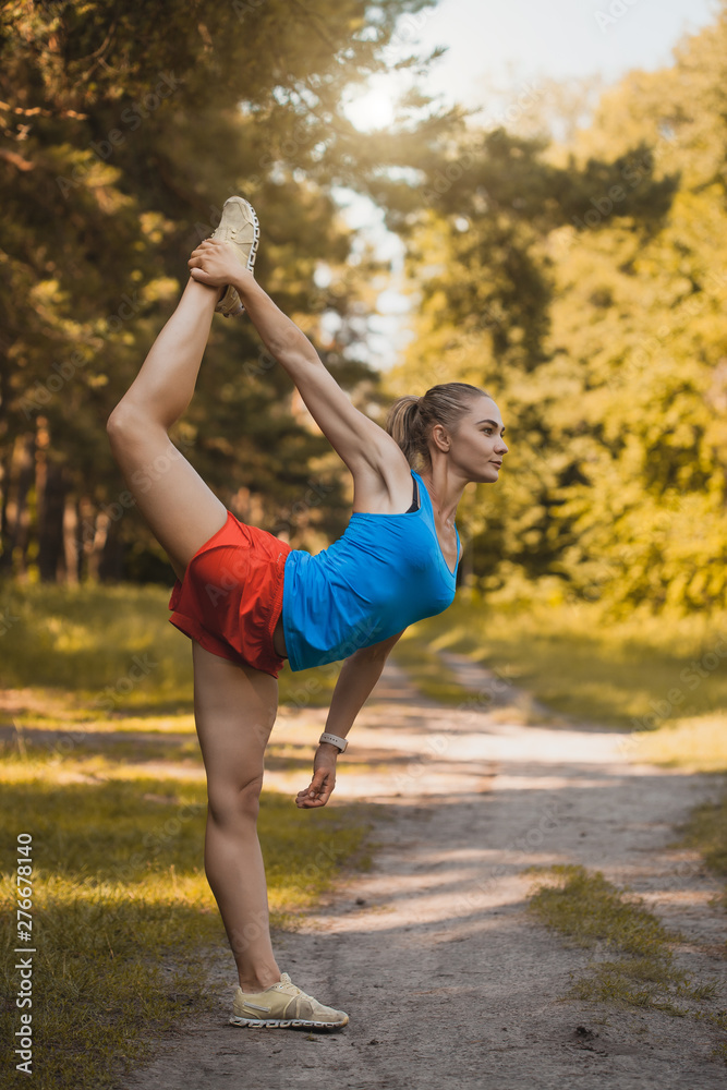 young woman is doing warming up before running in the park on a beautiful summer day