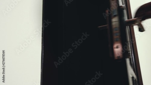 Brown wood door opens and man in a black leather jacket goes out and close door lock with key and goes away
