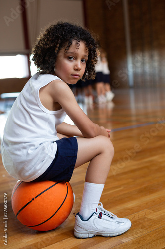 Schoolboy sitting on basketball and looking at camera