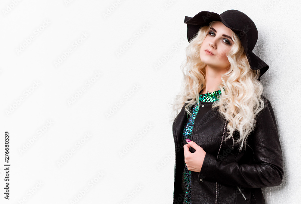 beautiful blonde girl in a brilliant dress and leather jacket posing against the white wall beautiful blonde girl in a brilliant dress and leather jacket posing against the white wall