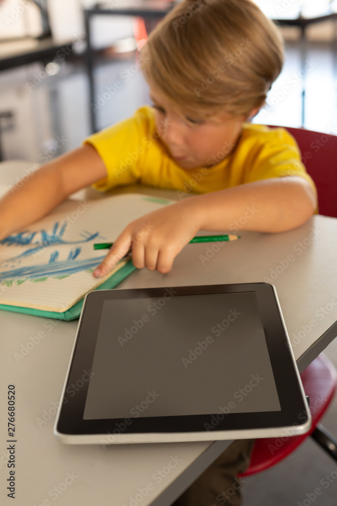 Boy drawing sketch on notebook at desk in a classroom Boy drawing sketch on notebook at desk in a classroom
