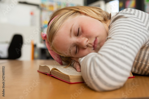 Schoolgirl sleeping on book at desk in the classroom